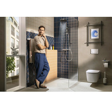 Salle de bains moderne avec douche à l'italienne, carrelage bleu foncé et beige et WC suspendu. Un homme se tient dans la pièce lumineuse.