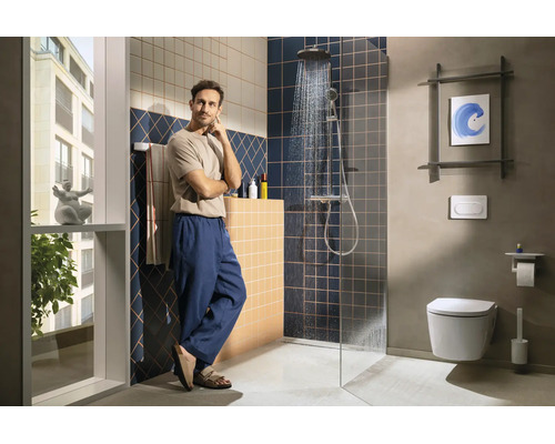 Salle de bains moderne avec douche à l'italienne, carrelage bleu foncé et beige et WC suspendu. Un homme se tient dans la pièce lumineuse.