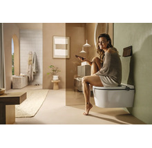 Femme assise sur des toilettes douche suspendues dans une salle de bains moderne et lumineuse, utilisant son smartphone.
