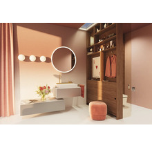 Salle de bains moderne et lumineuse avec lavabo suspendu, miroir LED rond, étagère en bois servant de cloison et accents roses comme le rideau et le pouf.