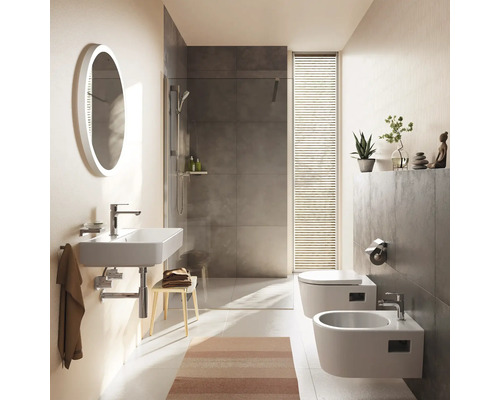 Salle de bains moderne avec lavabo mural, miroir ovale, douche à l'italienne aux carreaux gris, toilettes suspendues et bidet. Design lumineux.