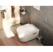 WC suspendu blanc avec abattant fermé dans une salle de bains moderne avec des carreaux sombres et des accessoires de salle de bains.