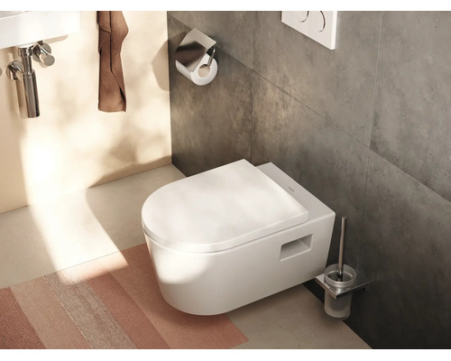 WC suspendu blanc avec abattant fermé dans une salle de bains moderne avec des carreaux sombres et des accessoires de salle de bains.