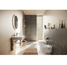 Salle de bains moderne avec lavabo suspendu, miroir lumineux ovale, douche à l'italienne avec carrelage gris, WC et bidet suspendus.