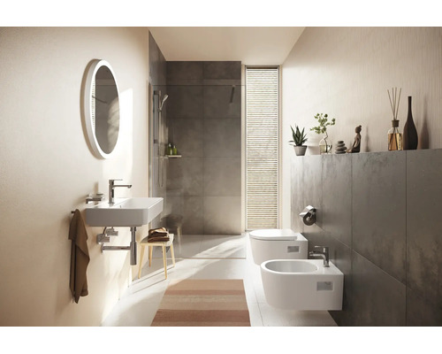 Salle de bains moderne avec lavabo suspendu, miroir lumineux ovale, douche à l'italienne avec carrelage gris, WC et bidet suspendus.