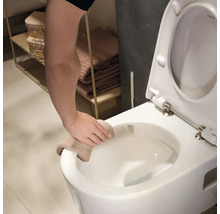 Une main nettoie le rebord de toilettes suspendues blanches avec un chiffon beige dans une salle de bains claire.