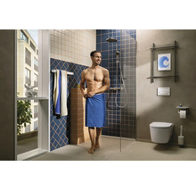 Salle de bains moderne avec douche à l'italienne, paroi en verre, toilettes suspendues, carreaux muraux à motifs et un homme avec une serviette.