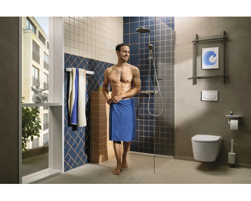 Salle de bains moderne avec douche à l'italienne, paroi en verre, toilettes suspendues, carreaux muraux à motifs et un homme avec une serviette.