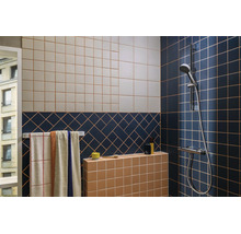 Salle de bains moderne avec des carreaux muraux à motifs bleus, beiges et terre cuite, un porte-serviettes et une robinetterie de douche chromée.