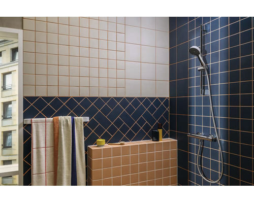 Salle de bains moderne avec des carreaux muraux à motifs bleus, beiges et terre cuite, un porte-serviettes et une robinetterie de douche chromée.