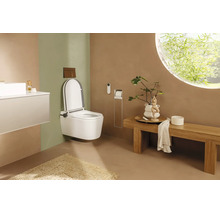 Salle de bains moderne avec WC douche suspendu blanc, banc en bois et fenêtre ronde. Design minimaliste aux tons terreux.
