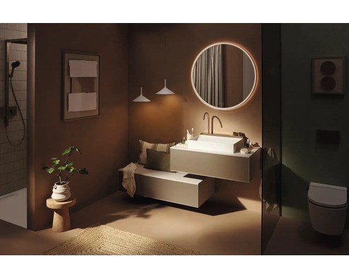 Salle de bains moderne avec miroir rond rétroéclairé, vasque à poser blanche sur meuble suspendu, espace douche et WC suspendu.