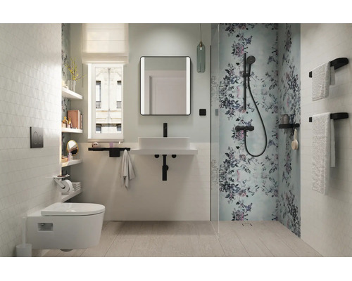 Salle de bains moderne et lumineuse avec WC suspendu, lavabo blanc, robinetterie noire et douche avec motif floral.