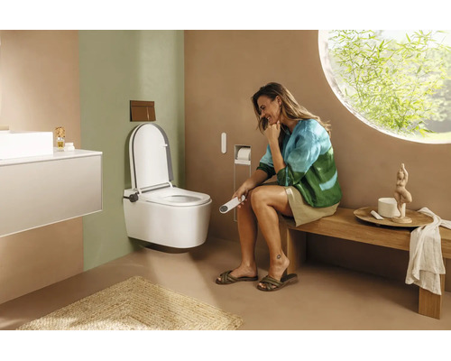 Salle de bains moderne avec WC lavant suspendu, femme assise sur un banc en bois tenant une télécommande et une fenêtre ronde.