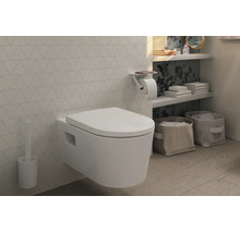 WC suspendu moderne avec abattant, brosse de toilette et porte-papier avec tablette dans une salle de bains lumineuse aux carreaux géométriques.