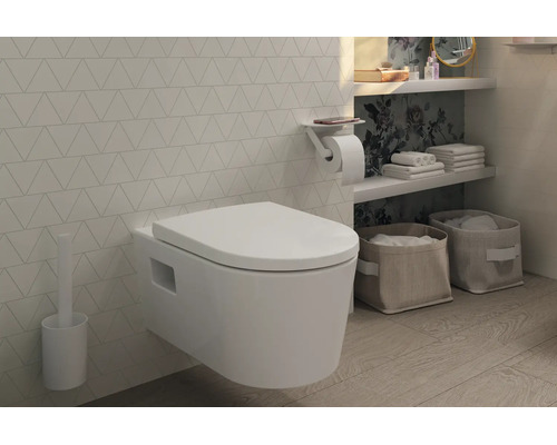 WC suspendu moderne avec abattant, brosse de toilette et porte-papier avec tablette dans une salle de bains lumineuse aux carreaux géométriques.