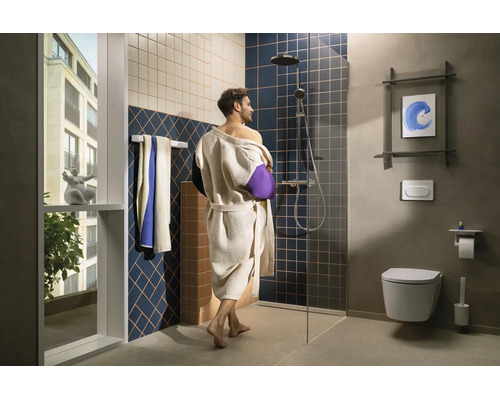 Salle de bain moderne avec personne en peignoir, douche à l'italienne, paroi en verre, WC suspendu, porte-serviettes et grande fenêtre.