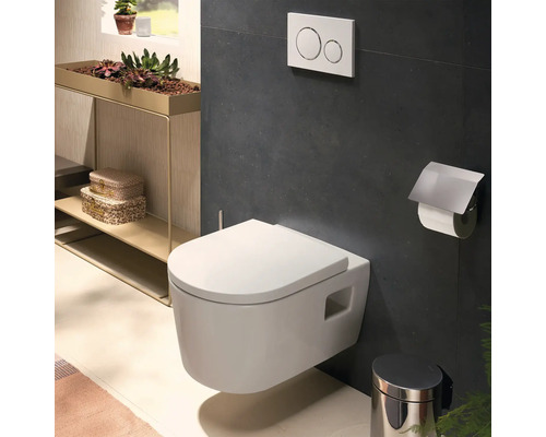 WC suspendu moderne dans une salle de bains avec plaque de déclenchement, porte-papier toilette et poubelle.