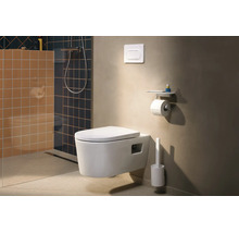 Salle de bains moderne avec WC suspendu, plaque de déclenchement, porte-rouleau avec tablette et brosse de toilette en blanc sur un mur beige.