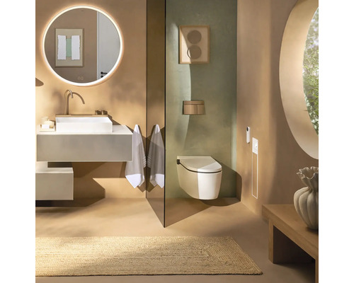 Salle de bains moderne avec vasque à poser blanche, miroir rond lumineux, WC suspendu et tapis naturel dans des tons terreux.