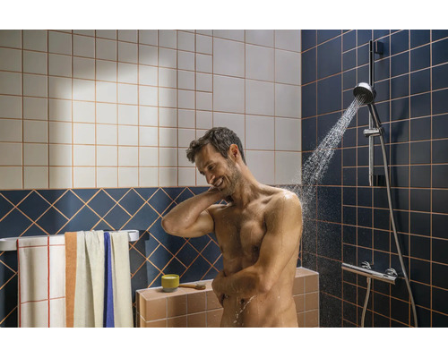 Homme se douchant sous une garniture de douche dans une salle de bains moderne avec carrelage et porte-serviettes.