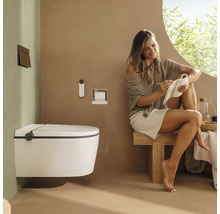 Salle de bains moderne avec toilette lavante suspendue, télécommande et plaque de déclenchement. Une femme est assise sur un banc en bois.