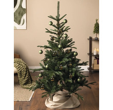 Sapin de Noël décoré dans un salon avec des boules vertes mates et brillantes et un cache-pied de sapin en tissu.