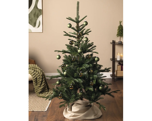 Sapin de Noël décoré dans un salon avec des boules vertes mates et brillantes et un cache-pied de sapin en tissu.