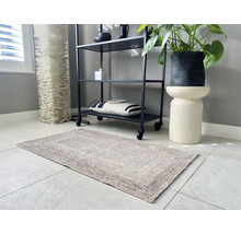 Tapis rectangulaire texturé dans une pièce moderne et lumineuse avec une étagère en métal noir, une plante en pot sur un socle et un sol carrelé.