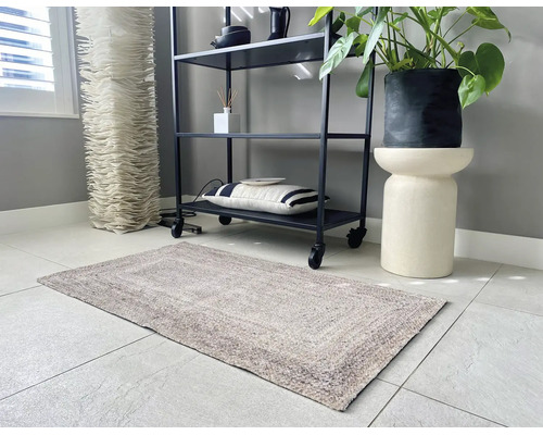 Tapis rectangulaire texturé dans une pièce moderne et lumineuse avec une étagère en métal noir, une plante en pot sur un socle et un sol carrelé.
