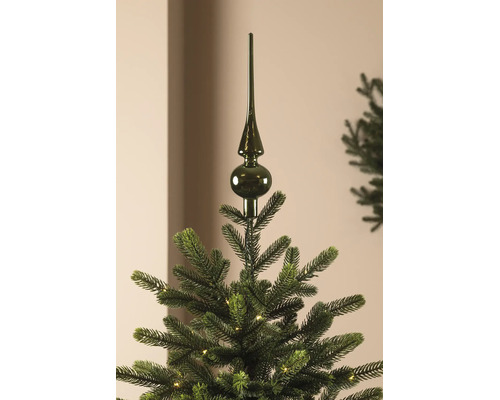Dunkelgrüne Christbaumspitze aus glänzendem Glas auf einem künstlichen Weihnachtsbaum mit Beleuchtung.