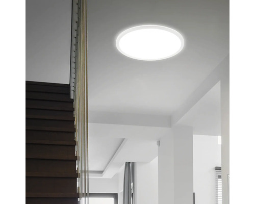 Flache runde LED-Deckenleuchte montiert in einem modernen hellen Treppenhaus mit Holzstufen.