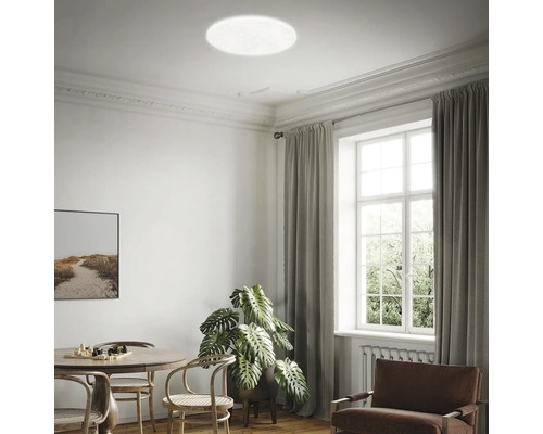 Helle, runde LED-Deckenleuchte in einem modern eingerichteten Wohnzimmer mit Esstisch, Zimmerpflanze und großem Fenster.