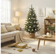 Sapin de Noël décoré de boules et d'une guirlande lumineuse dans un salon lumineux avec canapé, table basse et tapis.