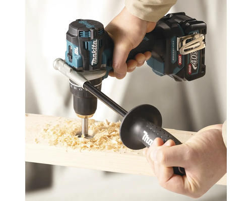 Perceuse-visseuse sans fil Makita 40 Volt avec poignée supplémentaire perçant un trou dans du bois avec des copeaux.