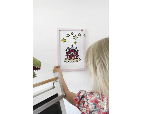 Ein Kind hält ein mit Glasmalfarbe gestaltetes Bild eines Schlosses in einem Rahmen an die Wand. Marabu Logo.