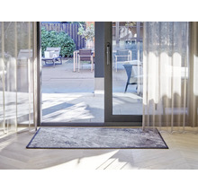 Paillasson rectangulaire aspect marbre devant une baie vitrée sur un parquet clair dans un intérieur moderne.