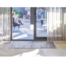 Tapis rectangulaire avec motif de planches de bois grises et bordure décorative dans un salon lumineux devant une baie vitrée coulissante.