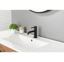 Mitigeur de lavabo noir moderne sur un lavabo blanc dans une salle de bains lumineuse avec une plante et une bougie.