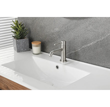 Lavabo moderne en céramique blanche avec mitigeur monocommande en métal brossé, plante grasse et bougie devant un mur en pierre.