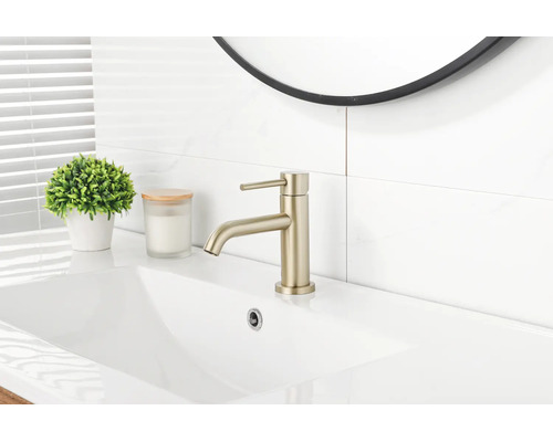 Mitigeur de lavabo monocommande moderne en or mat sur un lavabo en céramique blanc dans une salle de bains lumineuse.