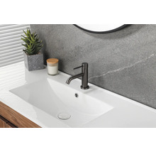 Salle de bains moderne avec lavabo blanc, mitigeur noir, mur gris aspect pierre et meuble sous vasque en bois.