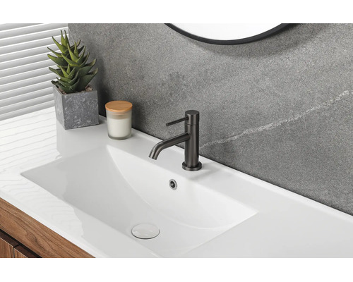Salle de bains moderne avec lavabo blanc, mitigeur noir, mur gris aspect pierre et meuble sous vasque en bois.