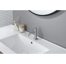 Mitigeur de lavabo moderne en métal brossé sur un lavabo blanc dans une salle de bains claire et organisée.