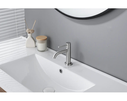 Mitigeur de lavabo moderne en métal brossé sur un lavabo blanc dans une salle de bains claire et organisée.
