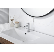 Mitigeur de lavabo chromé moderne sur un lavabo blanc dans une salle de bain lumineuse avec des carreaux effet marbre.