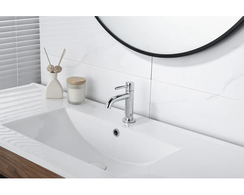 Mitigeur de lavabo chromé moderne sur un lavabo blanc dans une salle de bain lumineuse avec des carreaux effet marbre.