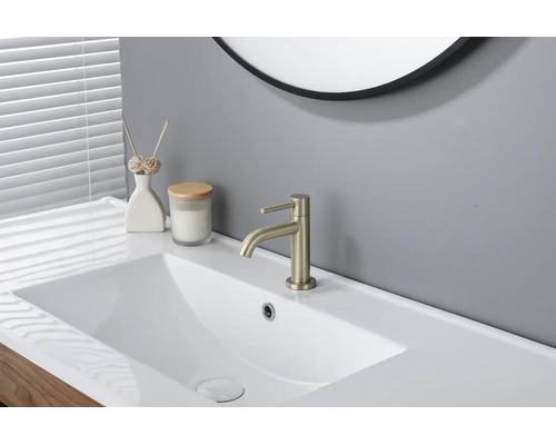 Salle de bain moderne lumineuse avec lavabo en céramique blanche, mitigeur doré et miroir rond.