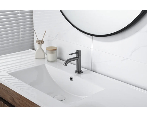 Salle de bains moderne et lumineuse avec lavabo rectangulaire blanc, mitigeur gris foncé, meuble sous-vasque en bois et carrelage aspect marbre.