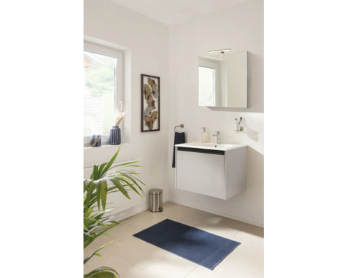 Salle de bain moderne avec meuble sous-lavabo suspendu blanc, armoire de toilette, robinet et tapis de bain bleu dans une pièce lumineuse.
